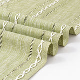 Close-up of sage-green woven runner and white embroidered detail.