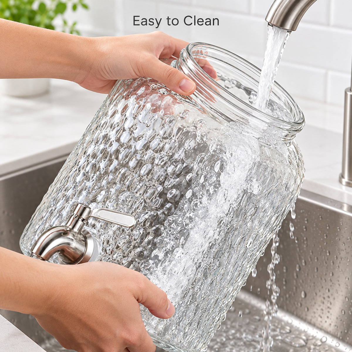A large clear glass beverage dispenser with a textured bubble pattern and a silver metal spout is being filled with running water in a kitchen sink. Hands are holding the glass, and the text 'Easy to Clean' appears at the top.