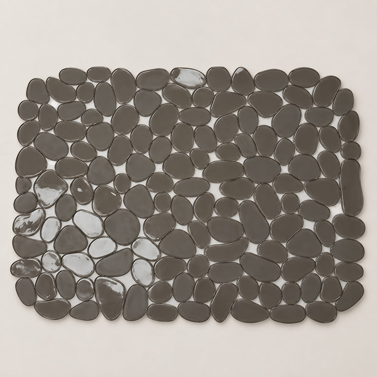 A rectangular bath mat made of smooth, dark gray pebble-shaped tiles, shown from a top-down view on a light beige background.