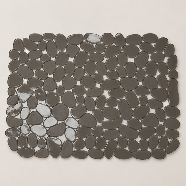A rectangular bath mat made of smooth, dark gray pebble-shaped tiles, shown from a top-down view on a light beige background.