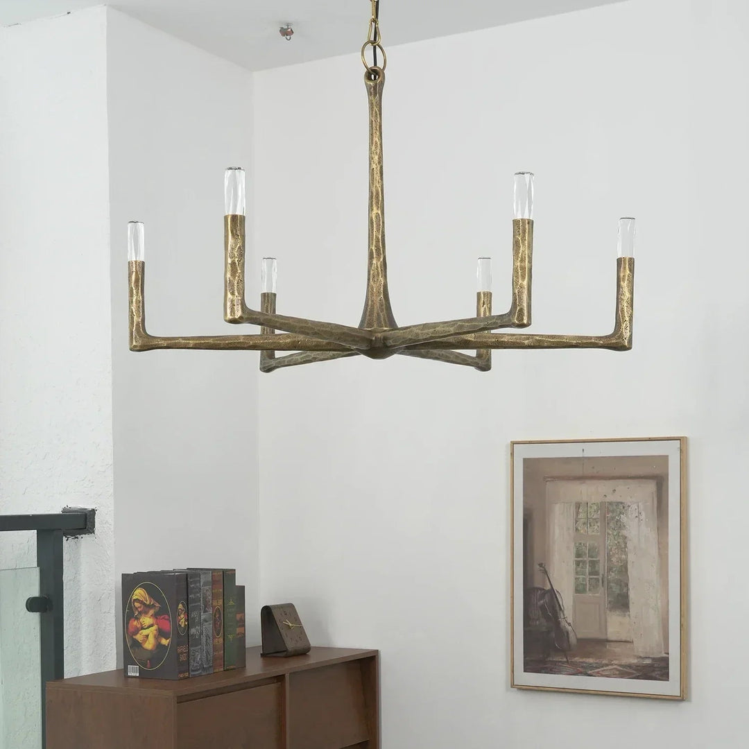 Brass chandelier hanging in a room with a wooden side table and framed picture on the wall.