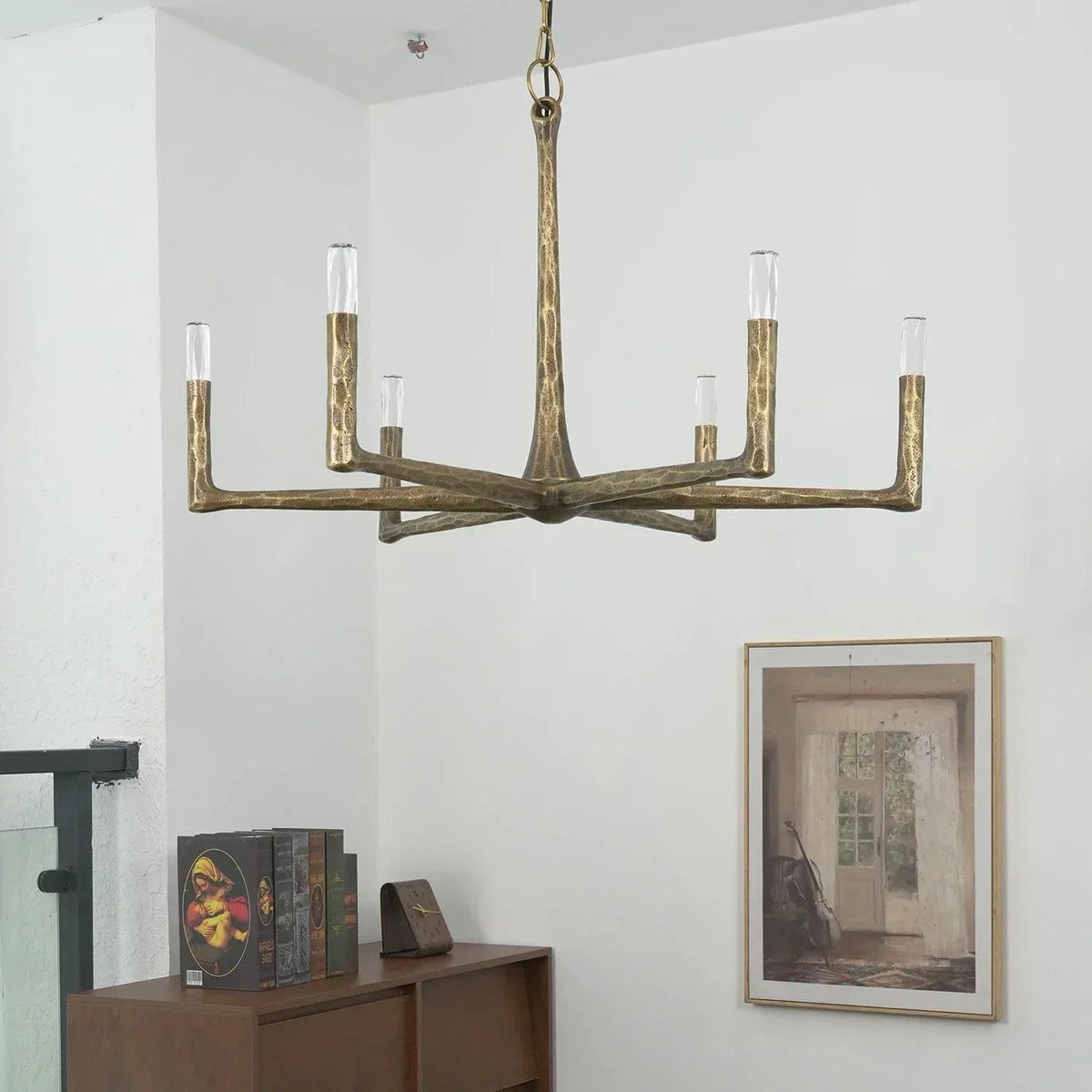 Brass chandelier hanging in a room with a wooden side table and framed picture on the wall.