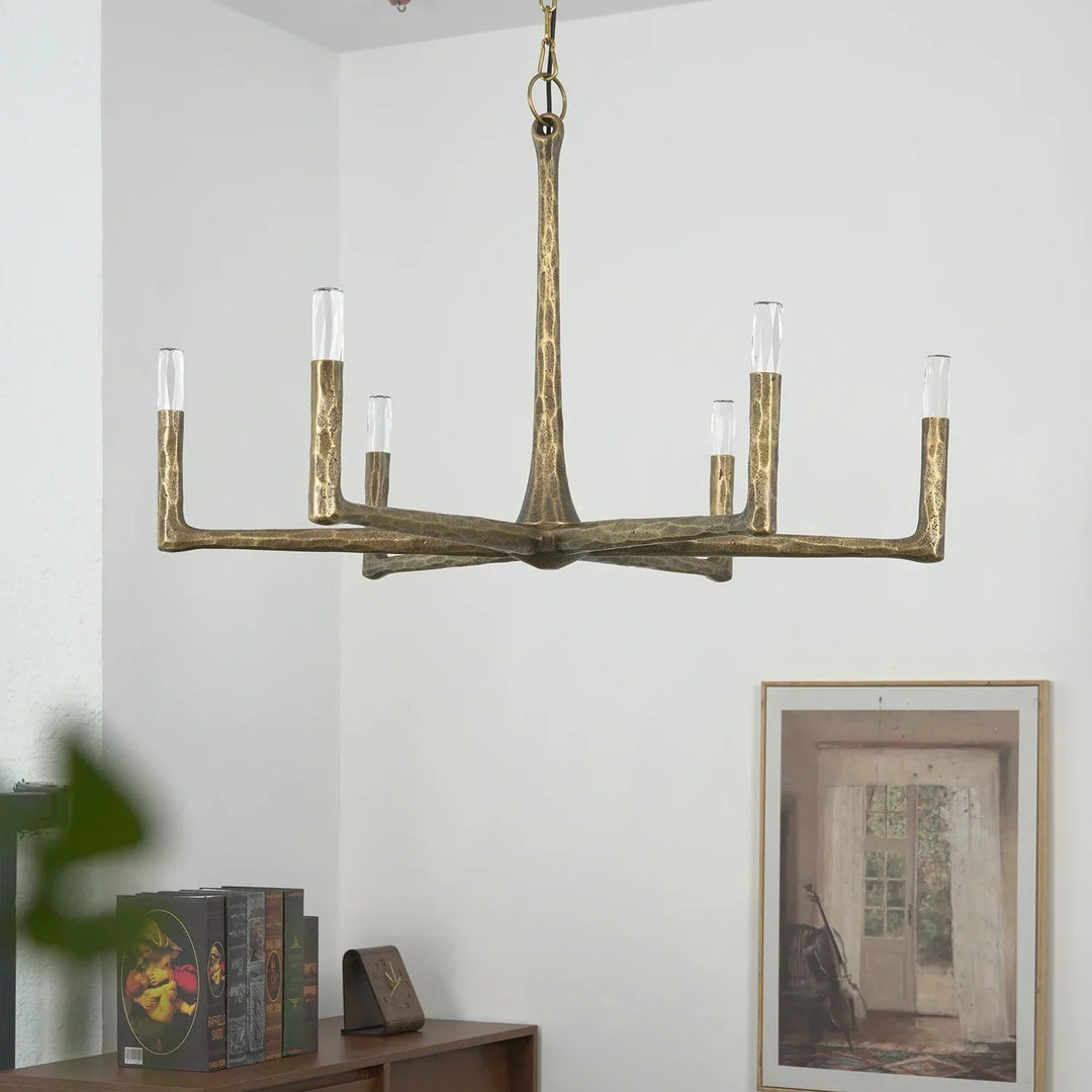 Brass chandelier hanging in a room with books and a painting on the wall.