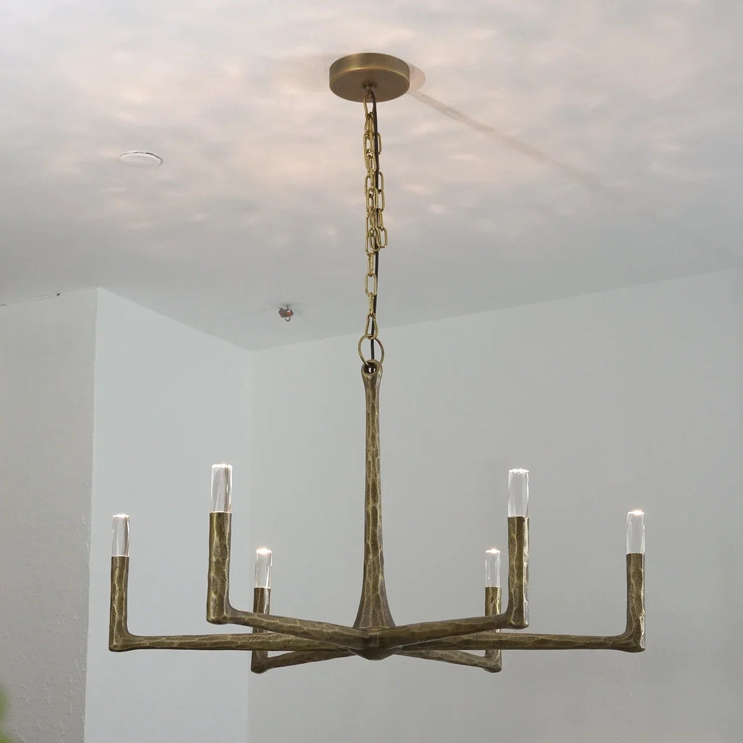 A six-light chandelier with a rustic, branch-like metal frame in a distressed bronze finish, suspended from a ceiling by a chain.