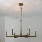 A six-light chandelier with a rustic, branch-like metal frame in a distressed bronze finish, suspended from a ceiling by a chain.
