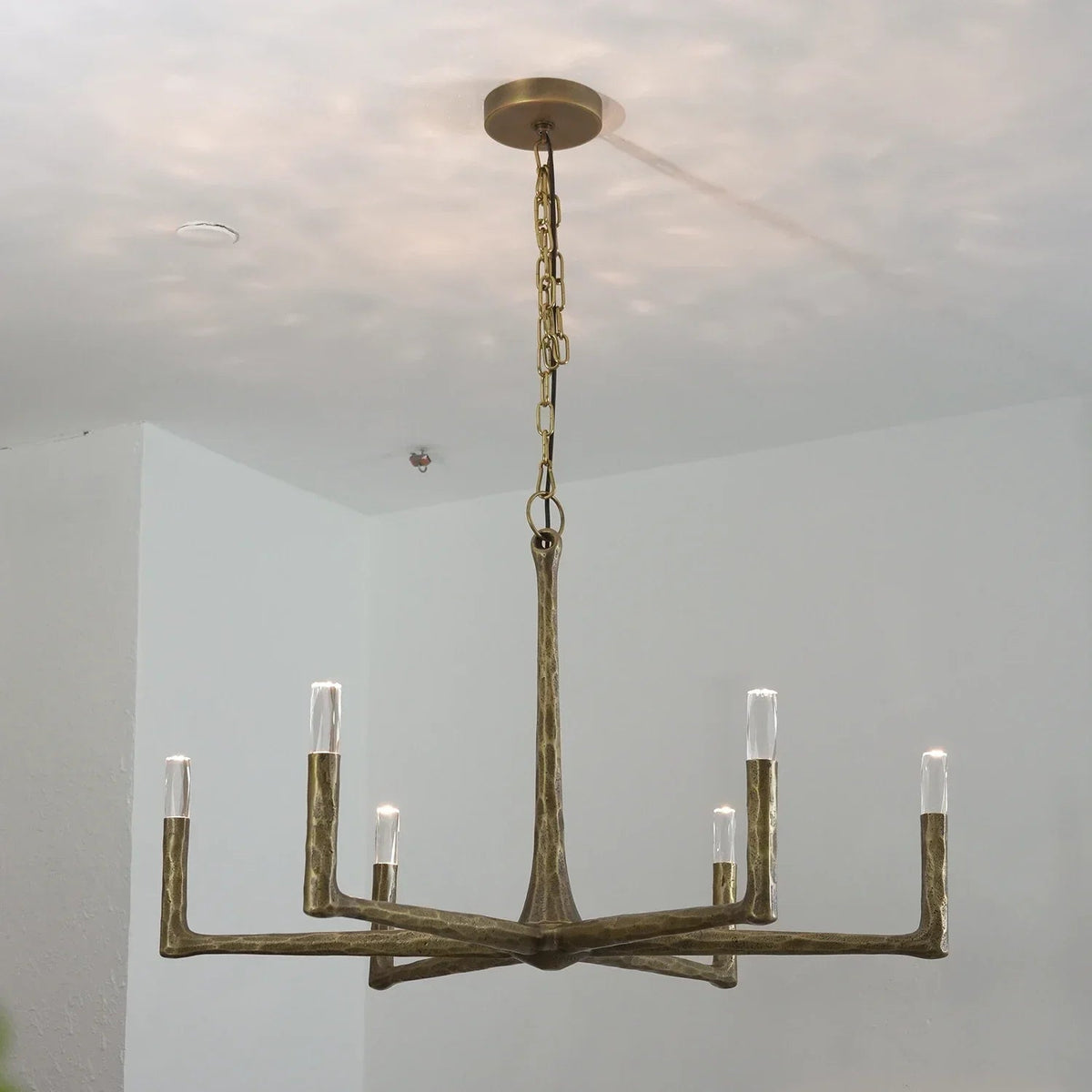 A six-light chandelier with a rustic, branch-like metal frame in a distressed bronze finish, suspended from a ceiling by a chain.