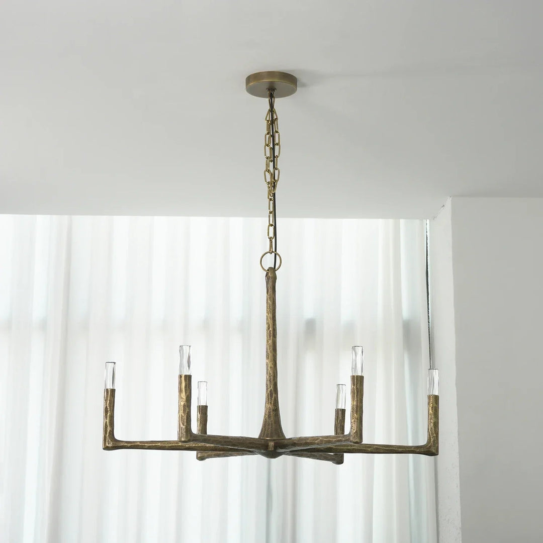 A rustic six-light chandelier with a weathered bronze finish hangs from a chain and ceiling canopy in a bright room with white curtains.