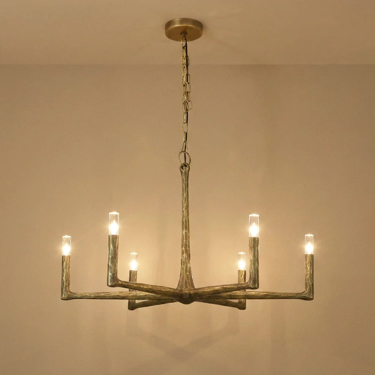 A rustic six-light chandelier with a weathered metal finish, suspended from a ceiling by a chain, shown against a plain beige wall.
