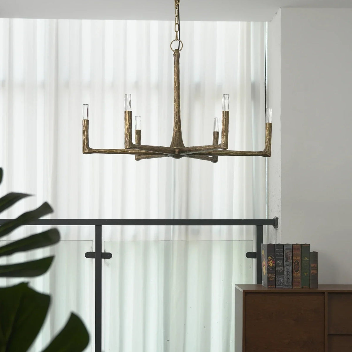 Bronze chandelier hanging in a room with a curtain and books on a shelf.