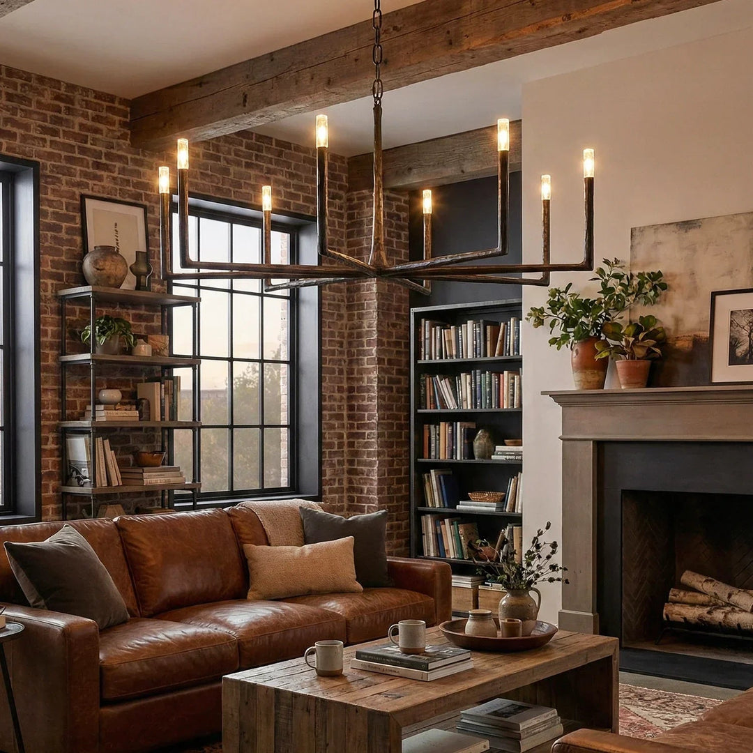Dark brass chandelier with branching arms and glowing crystal shades hangs above a leather sofa in a brick-walled living room.