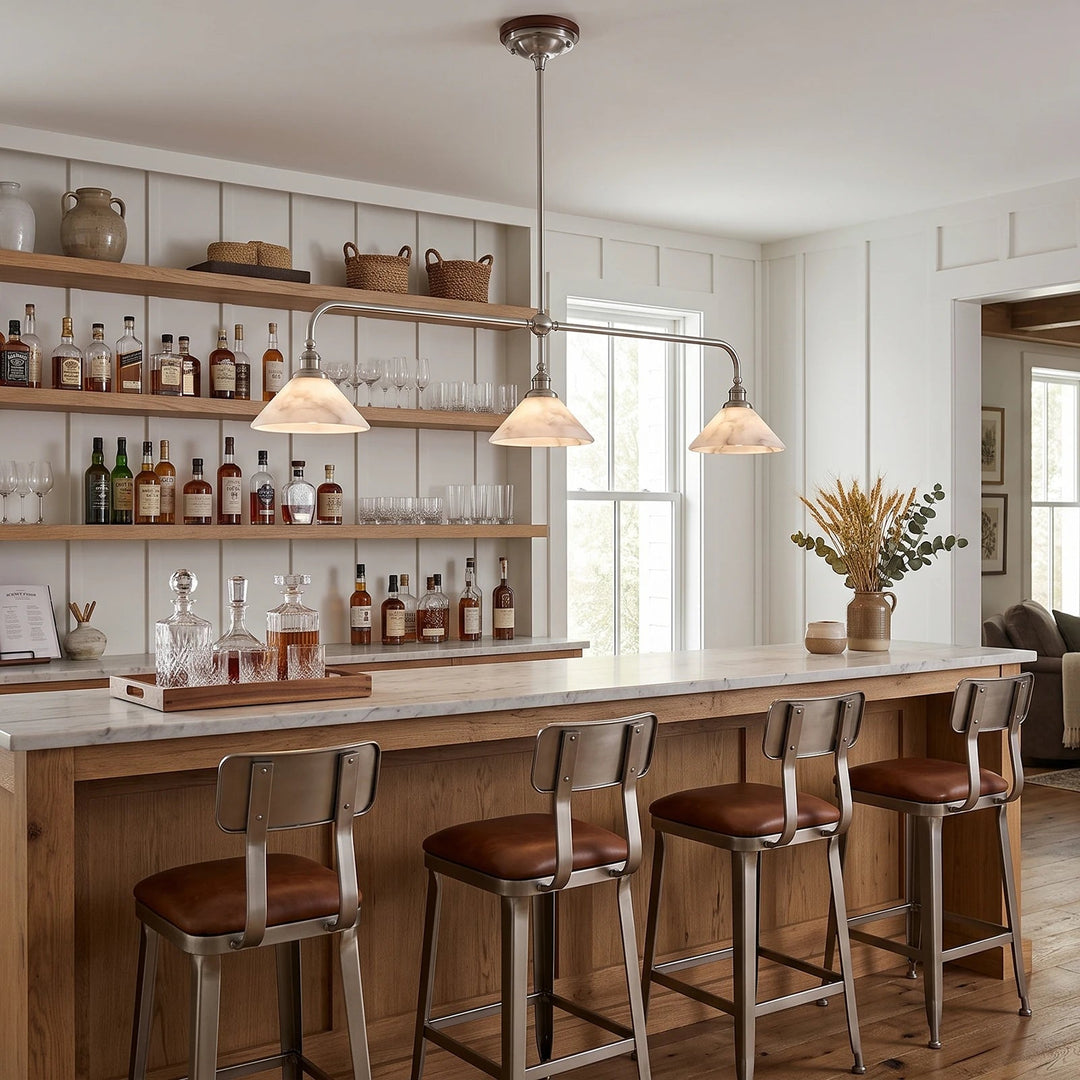 A pendant light with three glowing alabaster shades hangs above a wooden bar with open bottle shelves behind it.