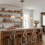 A pendant light with three glowing alabaster shades hangs above a wooden bar with open bottle shelves behind it.