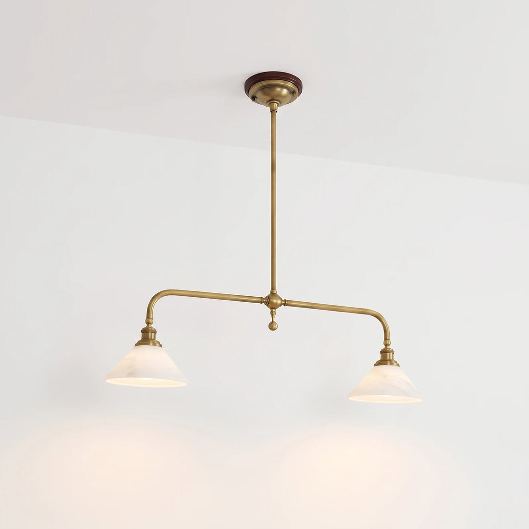 A brass pendant light with two pale alabaster shades casts warm pools of light against a plain white wall.