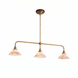 A brass pendant light with three illuminated, veined alabaster shades hangs against a white studio background.