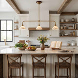 A modern kitchen interior with white cabinetry, a marble island, three wooden bar stools, a brass three-light pendant chandelier, exposed wood ceiling beams, and a white subway tile backsplash.