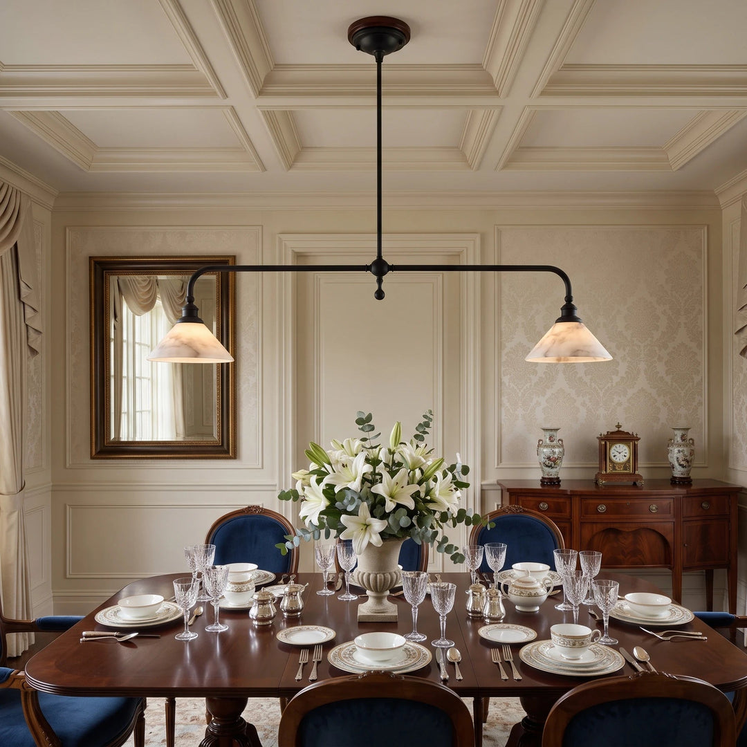A two-light linear pendant chandelier with black metal arms and warm beige glass shades hangs over a formal dining room table set with white dishes, wine glasses, and a floral centerpiece.
