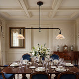 A two-light linear pendant chandelier with black metal arms and warm beige glass shades hangs over a formal dining room table set with white dishes, wine glasses, and a floral centerpiece.
