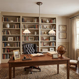A classic home office scene featuring a large wooden writing desk with a black tufted leather chair, set against a backdrop of built-in bookshelves filled with books. Two modern adjustable desk pendant lights hang over the desk, and a brown globe sits on the tabletop.