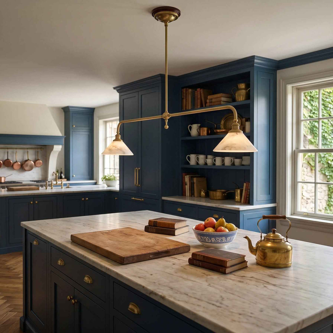 A brass multi-arm pendant light with two conical shades hangs over a kitchen island in a modern kitchen with dark blue cabinets and a marble countertop.
