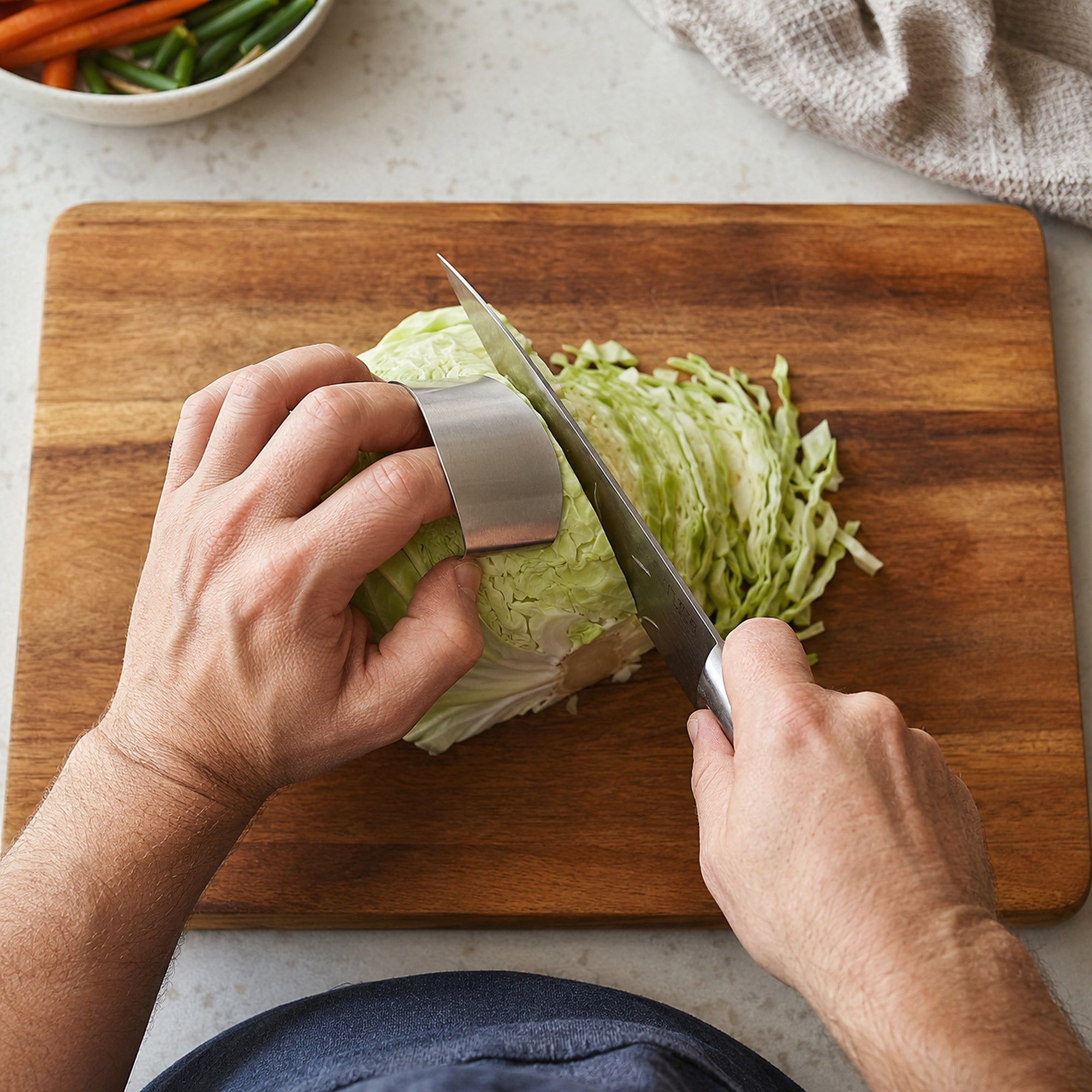 Hand wearing the stainless steel finger guard while a knife slices a wedge of cabbage on a wooden board