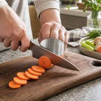 Stainless steel finger guard protecting the guiding hand while a chef knife cuts carrot rounds