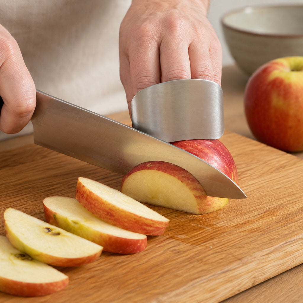 Stainless steel finger guard in use while a chef knife cuts an apple into wedges on a wooden board