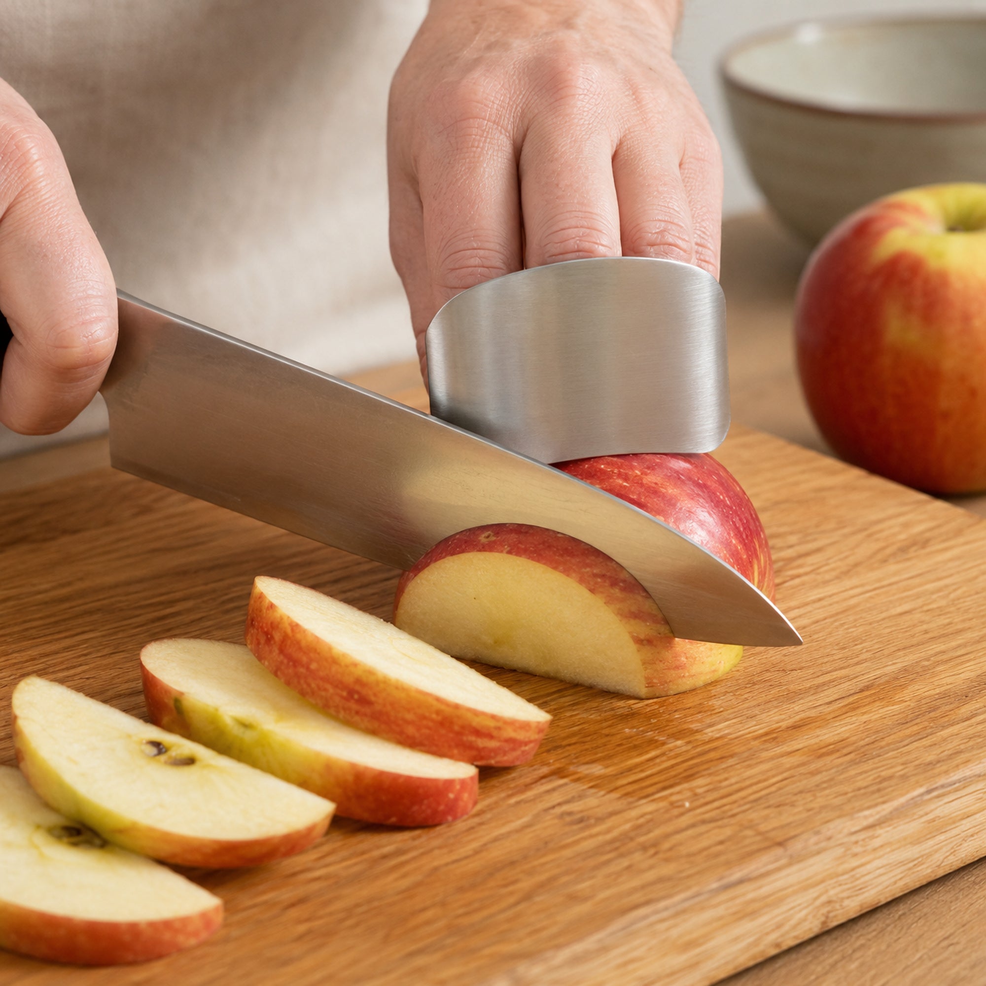 Stainless steel finger guard in use while a chef knife cuts an apple into wedges on a wooden board