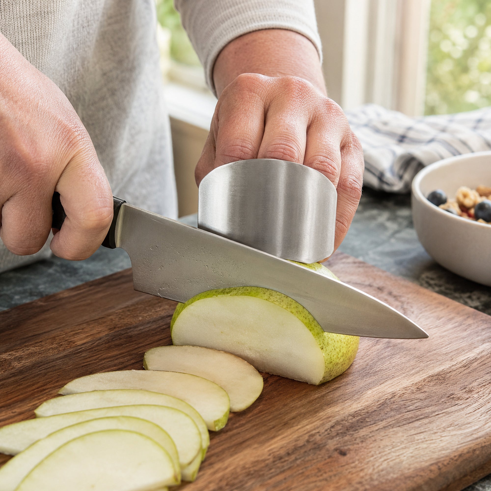 Stainless steel finger guard steadying a pear while a chef knife cuts even slices