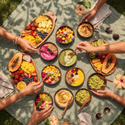 Overhead table of coconut bowls with fruit and dips, several hands reaching in