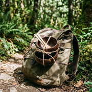 Two coconut bowls strapped to a canvas backpack on a forest trail