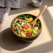 Coconut bowl filled with a green salad and cherry tomatoes, wooden spoon inside
