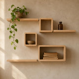 Light natural wood floating wall shelves mounted on a textured beige wall, styled with a trailing green plant, a small brown bottle, a ceramic bowl, and a stack of books.