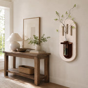 Design B cream capsule wall vase on a plain wall beside a console table and mirror