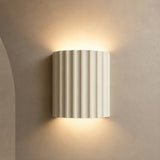 Ivory fluted up down wall sconce lit warm on a greige wall