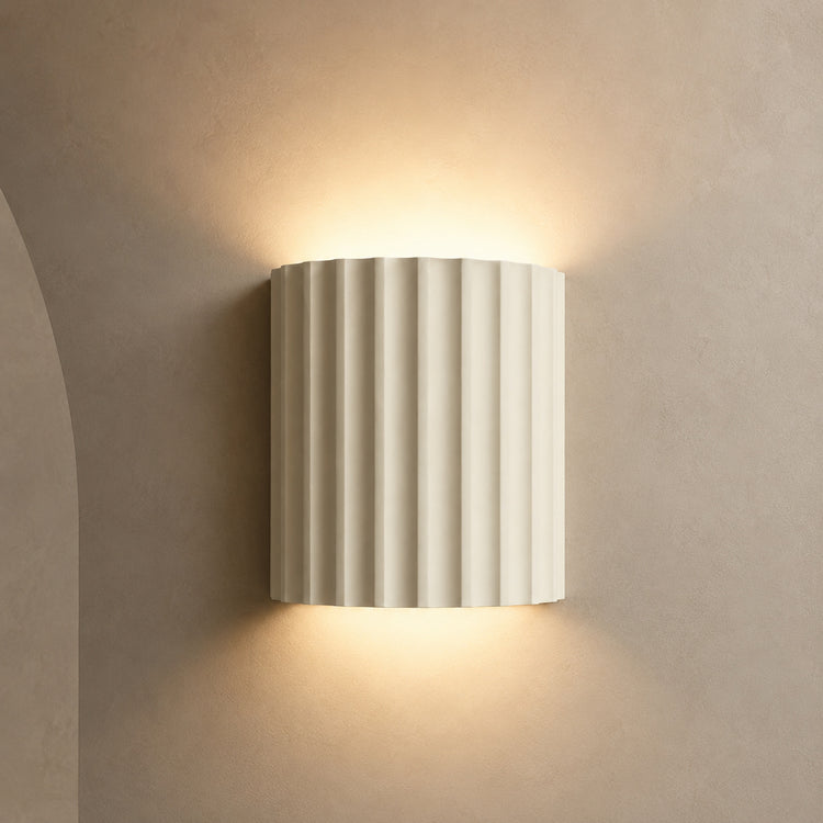 Ivory fluted up down wall sconce lit warm on a greige wall
