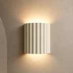 Ivory fluted up down wall sconce lit warm on a greige wall