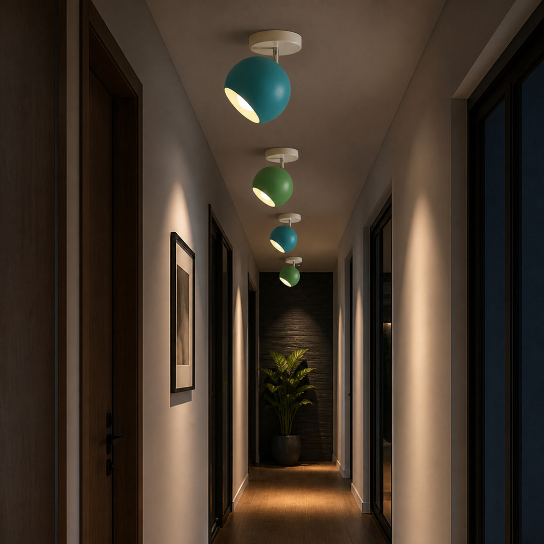 A hallway with four modern ceiling lights in a row, each featuring a spherical shade in teal and mint green with a white top mount. The lights cast a warm yellow light downward onto the wooden floor, with dark wood doors lining both sides of the corridor.