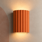 Terracotta ribbed wall sconce lit up and down on a plaster wall