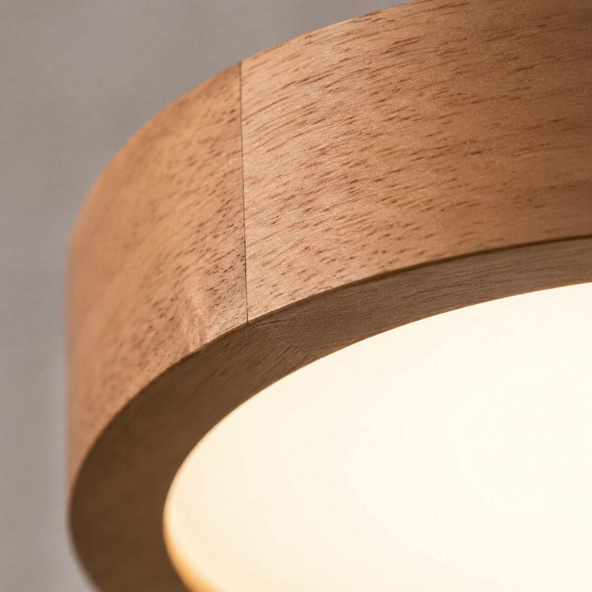 Close-up of a modern cylindrical pendant light with a natural wood frame and a glowing warm white frosted glass shade.