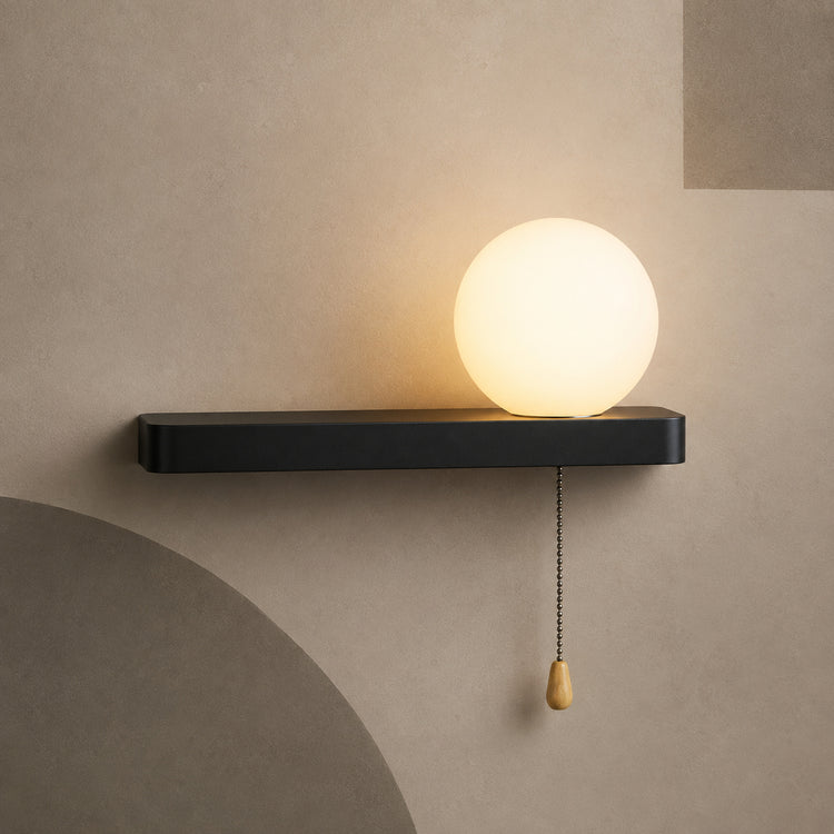 Matte black bar globe wall sconce lit warm with pull chain switch