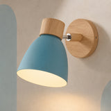 A modern wall-mounted light fixture with a matte blue cone-shaped shade, natural wood accents, and a round wooden wall plate, shown lit against a textured beige wall.