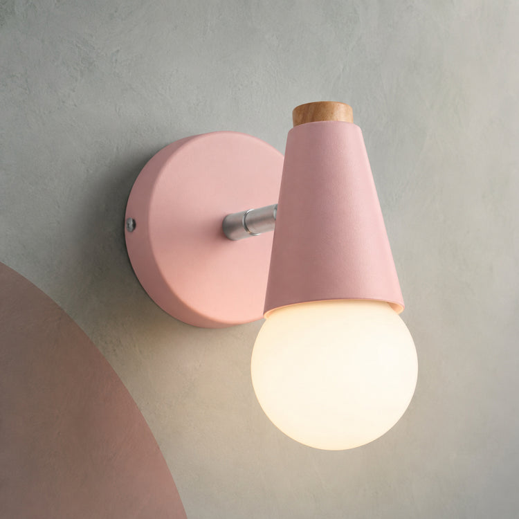 Pink small wall sconce lit warm on a gray wall with blush shapes