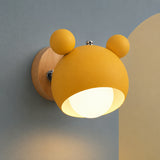 A yellow bear-shaped wall sconce with a warm glowing light, mounted on a wooden backplate against a split gray and beige wall.