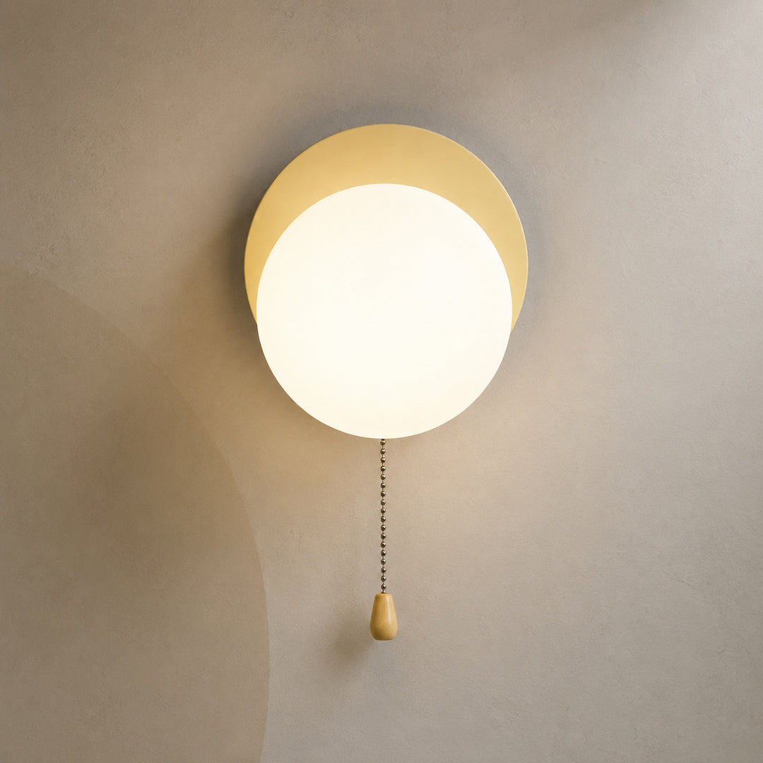 Soft beige disc globe wall sconce lit warm with pull chain switch
