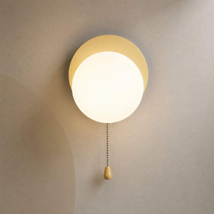 Soft beige disc globe wall sconce lit warm with pull chain switch