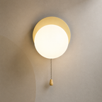 Soft beige disc globe wall sconce lit warm with pull chain switch