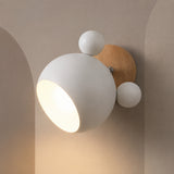 A modern wall sconce light fixture with a matte white spherical shade, two smaller white spherical accents, and a round natural wood backplate mounted on a beige wall.