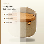 A ceramic salt cellar with a speckled beige body and a light brown wooden lid, shown on a clean off-white background with text listing features like 'Open scoop', 'Counter ready', and 'Tray on sets'.