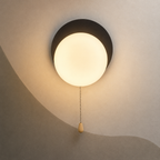 Matte black disc globe wall sconce lit warm with pull chain switch