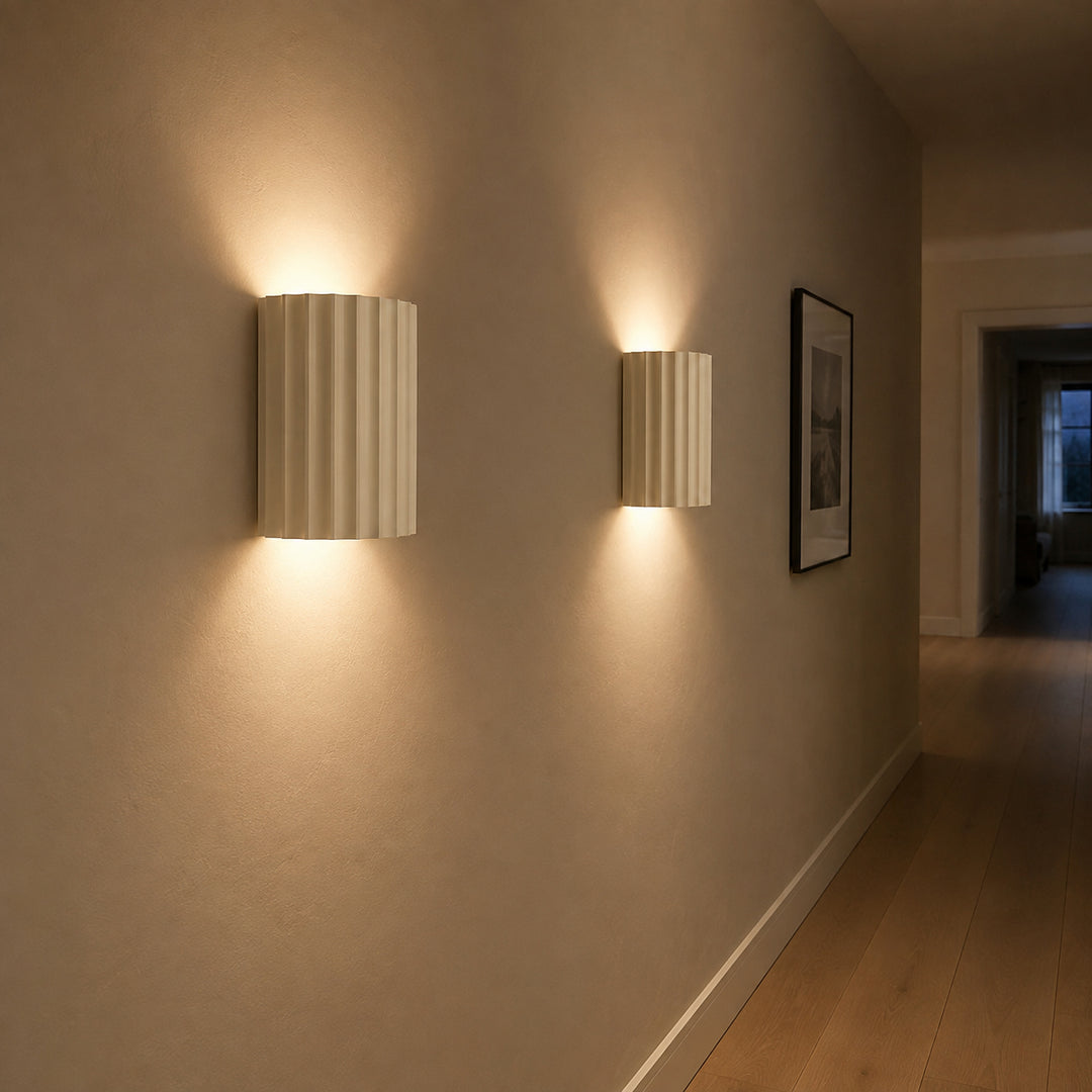 Two ivory fluted up down wall sconces lighting a narrow hallway with oak flooring